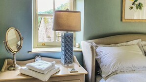 Une chambre à coucher avec un lit, une table de chevet avec une lampe, un miroir et une fenêtre donnant sur un paysage verdoyant.