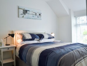 Quarto com cama, mesas de cabeceira, abajur e janela com persianas.