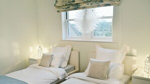 Ein Doppelzimmer mit zwei Einzelbetten, weißer Bettwäsche und einem Fenster mit weißem Vorhang.