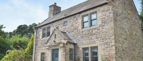 A stone house with a gabled roof, a chimney, and a front door.