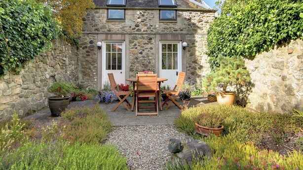 A stone house with a garden, a wooden table and chairs, and a gravel path. - 2 bedroom accommodation in Linlithgow, near Edinburgh (Linlithgow, near Edinburgh)