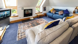 A modern living room with a flat-screen TV, a fireplace, a blue sofa, and a patterned rug. - 2 bedroom accommodation in Linlithgow, near Edinburgh (Linlithgow, near Edinburgh)