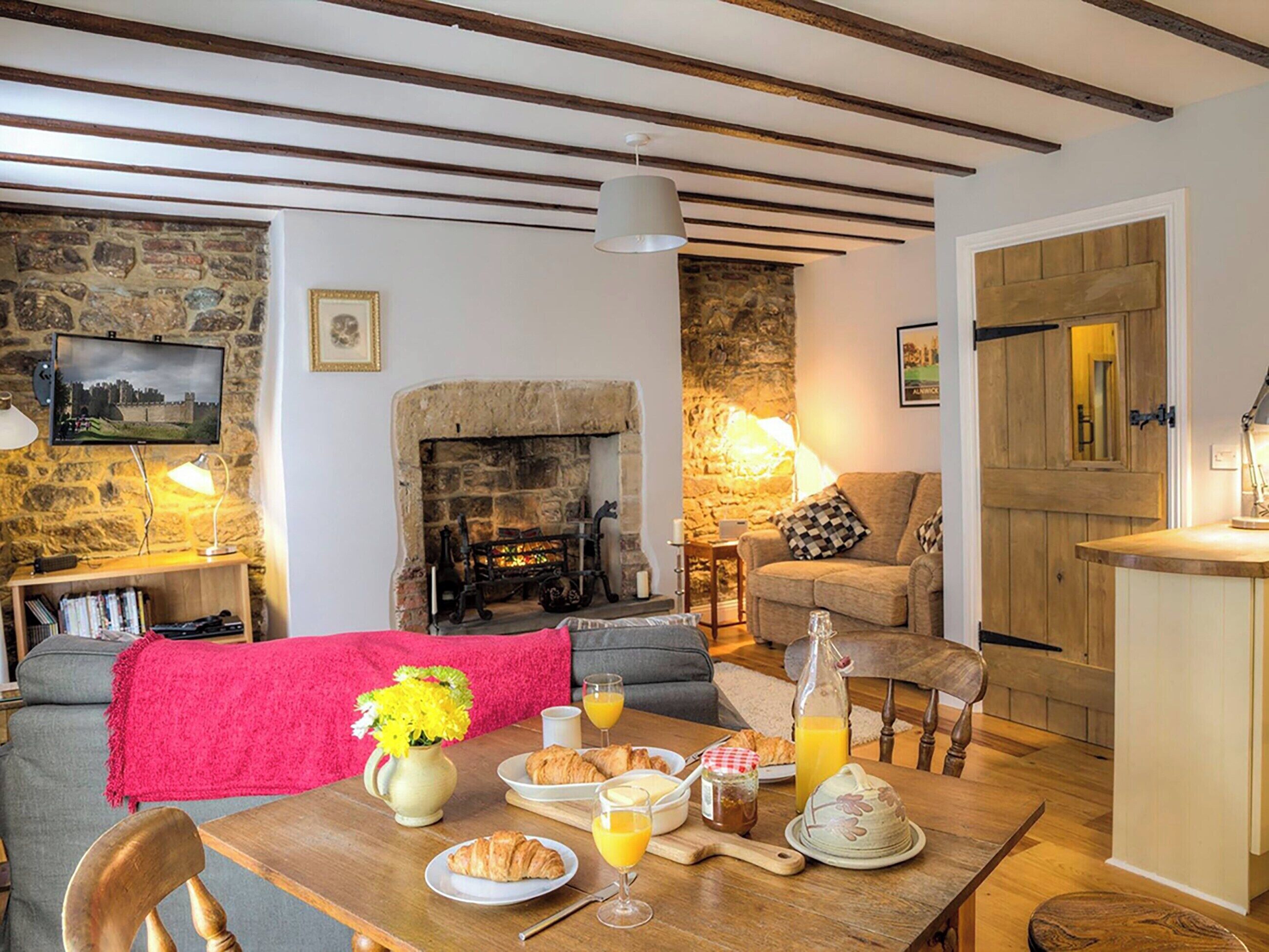 A cozy living room with a stone fireplace, a wooden table set for breakfast, and a comfortable sofa.
