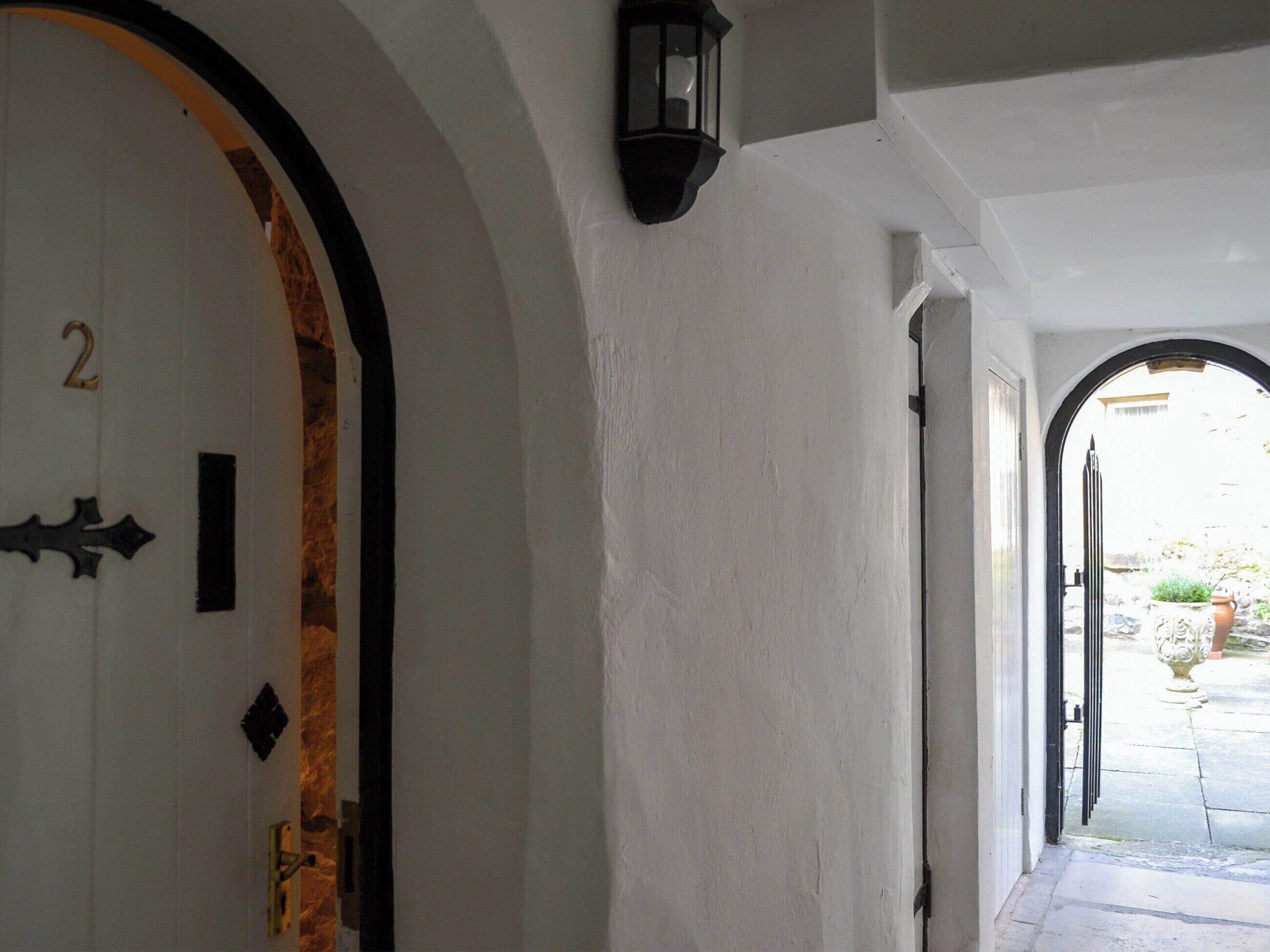 A hallway with white walls, a door with a number '2' and a black decorative element, and a black lantern on the wall.