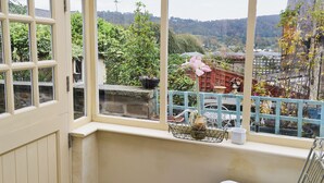 Une pièce dotée d’une grande fenêtre, d’un lit, d’une chaise et offrant une vue sur un jardin et des bâtiments.
