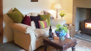 Un salon avec un canapé, une table basse en bois, un vase de fleurs, une lampe et une cheminée.