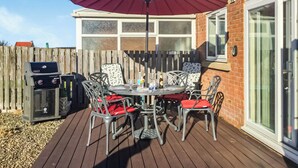 Une terrasse extérieure avec une table et des chaises, un barbecue et un grand parasol.