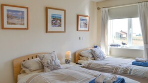 Une chambre d’hôtel avec deux lits, une fenêtre avec des rideaux et trois tableaux encadrés accrochés au mur.