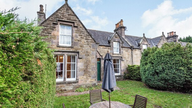 A stone house with a garden patio featuring a round wooden table and four chairs, surrounded by greenery. - 2 bedroom accommodation in Keith (Keith)