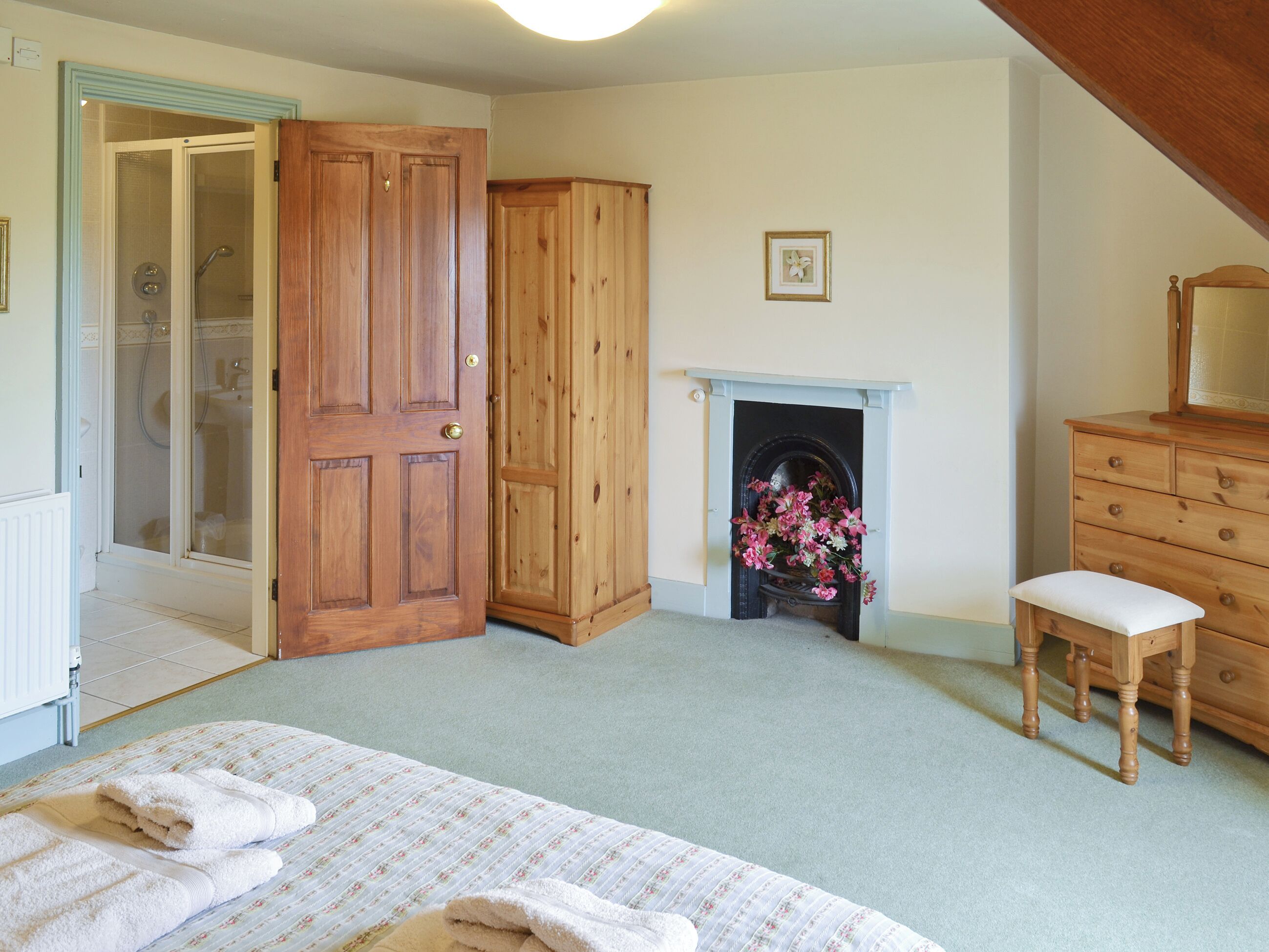 A bedroom with a bed, a wooden wardrobe, a dresser, a fireplace, and a shower area.