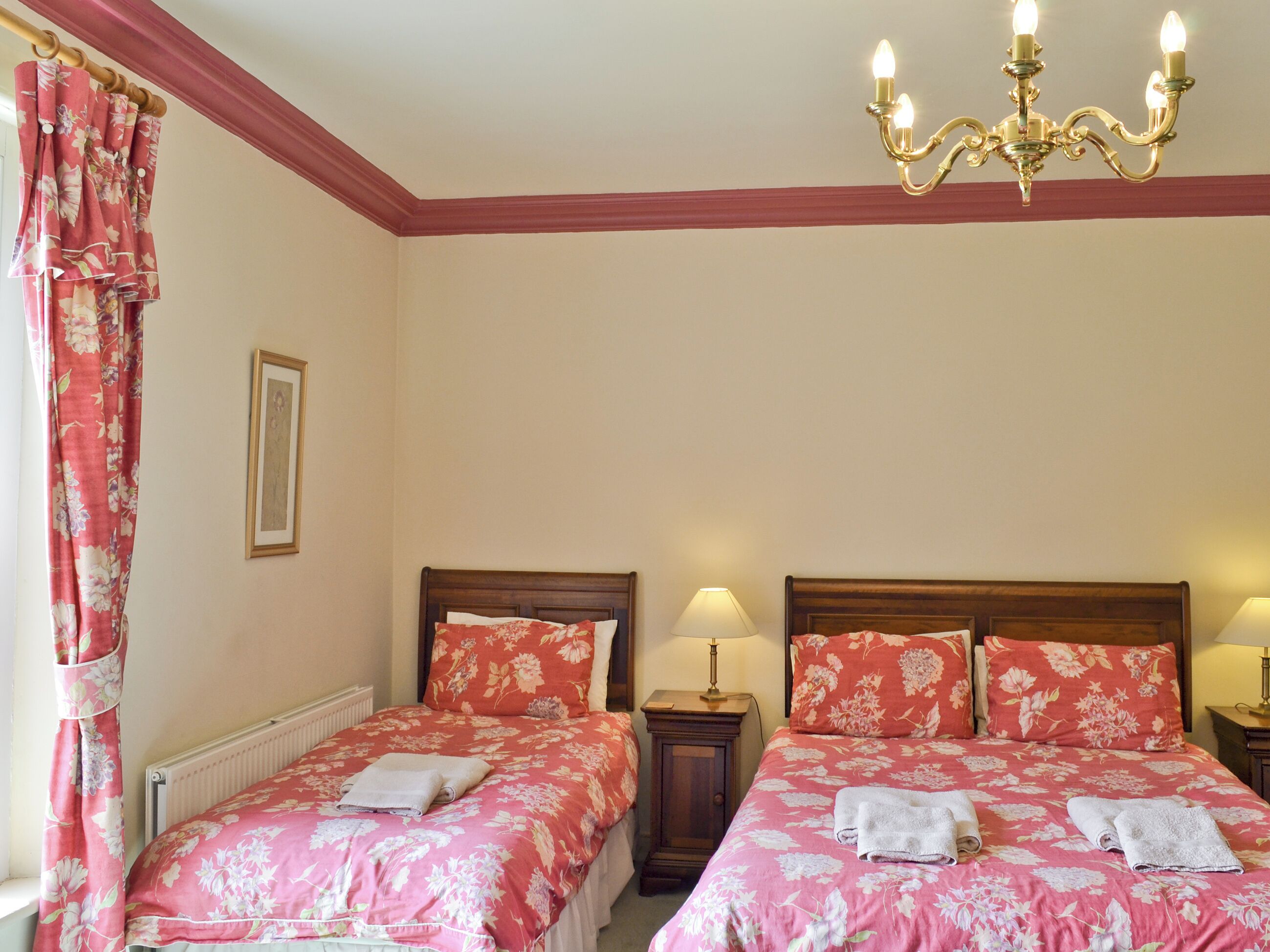 Habitació doble amb dos llits, cadascun amb roba de llit i tovalloles florals, una làmpada de cristall i un quadre a la paret.
