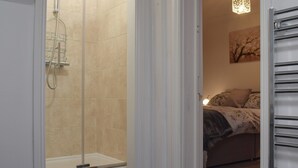 Une salle de bain moderne avec une douche à parois de verre, un lit avec une literie à motifs floraux et un luminaire décoratif.