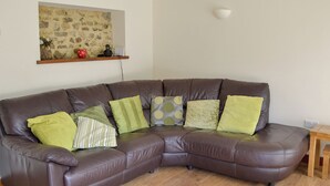 A brown leather sectional sofa with five cushions, a stone wall with a painting, and a small table with a light fixture. - Nestled in the Blackdown Hills, this barn is secluded and secure dog-friendly. (Dunkeswell Abbey, near Honiton)