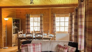 A cozy cabin interior with a dining area, a sofa with plaid cushions, and a wooden ceiling.