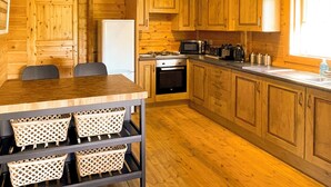 A wooden cabin interior with a kitchen area, including a dining table, chairs, a refrigerator, a stove, and cabinets.