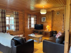 A wooden cabin interior with a sofa, a television, a lamp, and plaid curtains. - Sun Rise Lodge No 10 - HW7655 (Llanbedr)