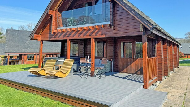 A wooden cabin with a large glass window, a deck with lounge chairs, and a clear sky.
