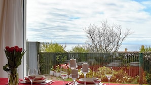 A dining table set for four with a red tablecloth, white plates, and wine glasses, overlooking a garden with a view of the sea. - 4 bedroom accommodation in St Monans, near Anstruther (St Monans, near Anstruther)