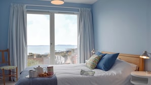 A bedroom with a bed, a bedside table, a lamp, a chair, and a view of the sea. - 4 bedroom accommodation in St Monans, near Anstruther (St Monans, near Anstruther)