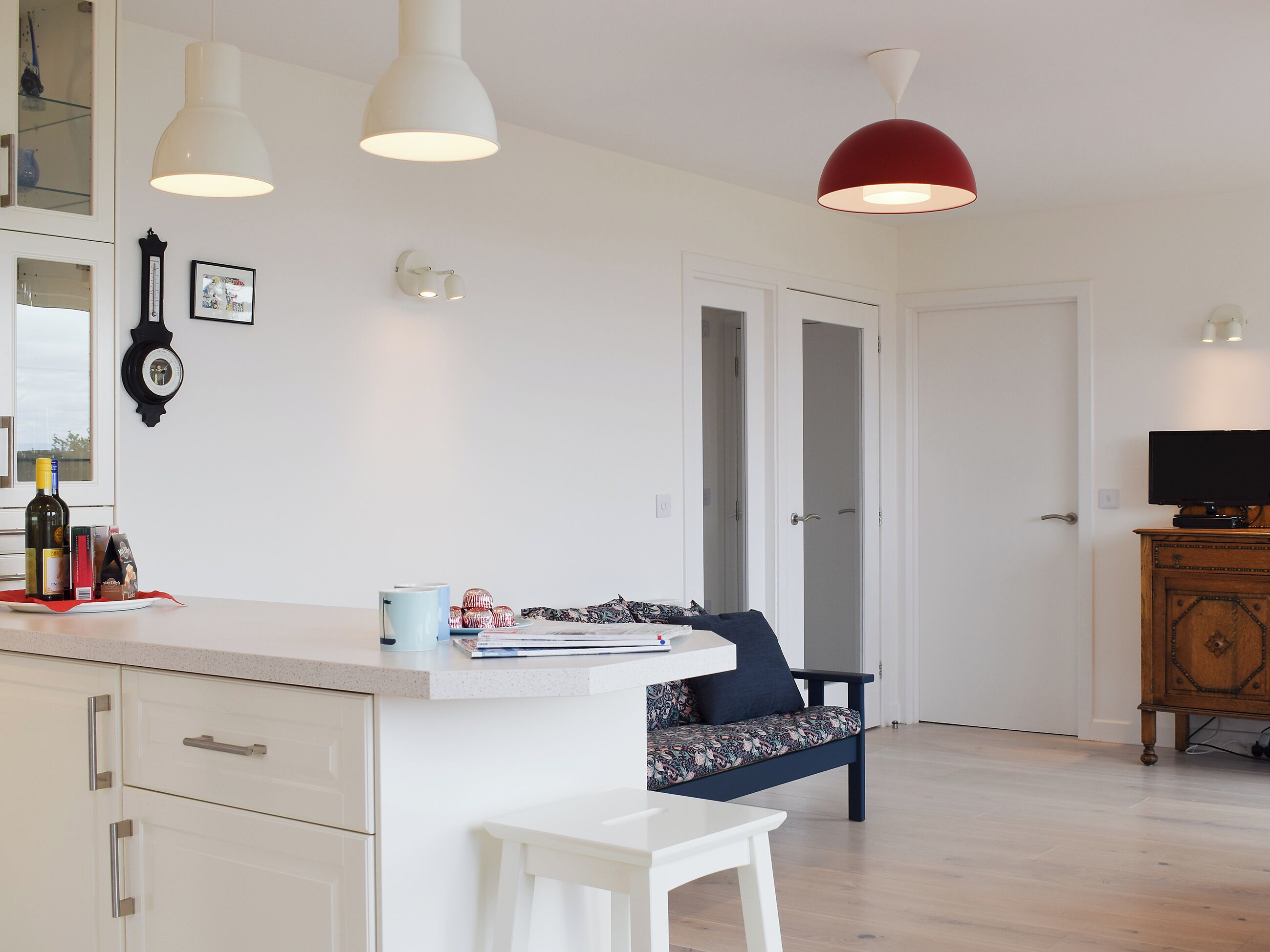 Una cocina moderna con armarios blancos, un comedor con banco y un televisor sobre un mueble de madera.