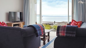A living room with a television, two sofas, a table, and a view of the sea. - 4 bedroom accommodation in St Monans, near Anstruther (St Monans, near Anstruther)