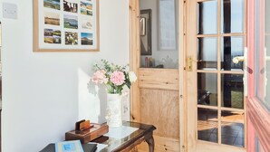 Una puerta de madera con paneles de vidrio, una mesita con un florero y una pared decorada con fotografías enmarcadas.