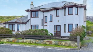 Una casa de dos pisos con fachada de piedra, múltiples ventanas y techo con paneles solares.