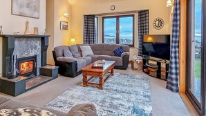 Una sala de estar con chimenea, un sofá, un televisor y vistas al exterior.