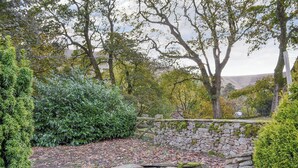 A stone wall with a wooden gate, surrounded by dense greenery and trees.