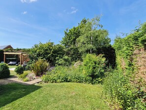 Un jardin agrémenté d’une pergola, d’une pelouse et de divers arbustes et arbres.