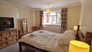Ein Schlafzimmer mit einem Bett, einem Fernseher, einer Lampe, einem Fenster mit Vorhängen und einem Sessel.