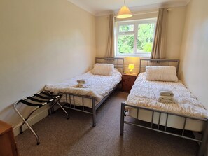 Une chambre avec deux lits simples, une petite table de chevet avec une lampe, une chaise et une fenêtre avec des rideaux.