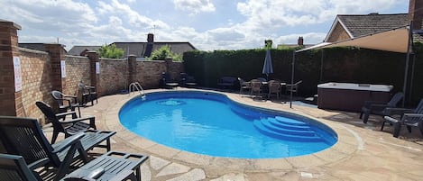 A swimming pool with lounge chairs and a hot tub in a backyard setting.