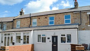 Ein zweistöckiges Wohngebäude mit weißer Vorderfront, mehreren Fenstern und einer schwarzen Tür.