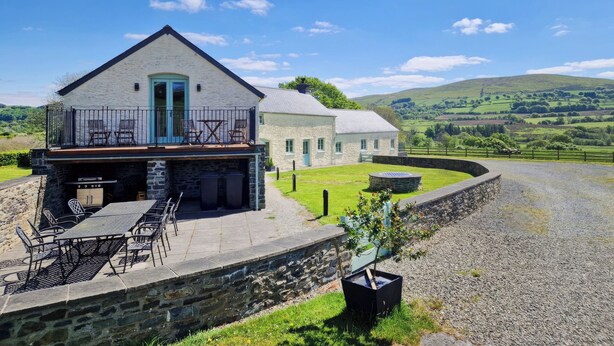 A stone house with a balcony, outdoor seating, and a view of rolling hills. - Felin Hedd (Peaceful Mill) (Tregaron, near Aberystwyth)