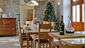 A dining area with a wooden table, chairs, a Christmas tree, and a bottle of Porto Armilar Ruby Port. - Felin Hedd (Peaceful Mill) (Tregaron, near Aberystwyth)