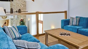 A modern living room with a wooden ceiling, a stone wall, a blue sofa, a wooden coffee table, and a Christmas tree. - Felin Hedd (Peaceful Mill) (Tregaron, near Aberystwyth)