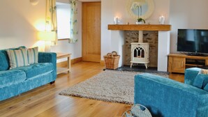 A living room with a stone fireplace, a television, and two blue sofas. - Felin Hedd (Peaceful Mill) (Tregaron, near Aberystwyth)