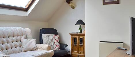 En hyggelig stue med højt til loftet, en sofa, en lænestol, et træskab, et bord og et fjernsyn.
