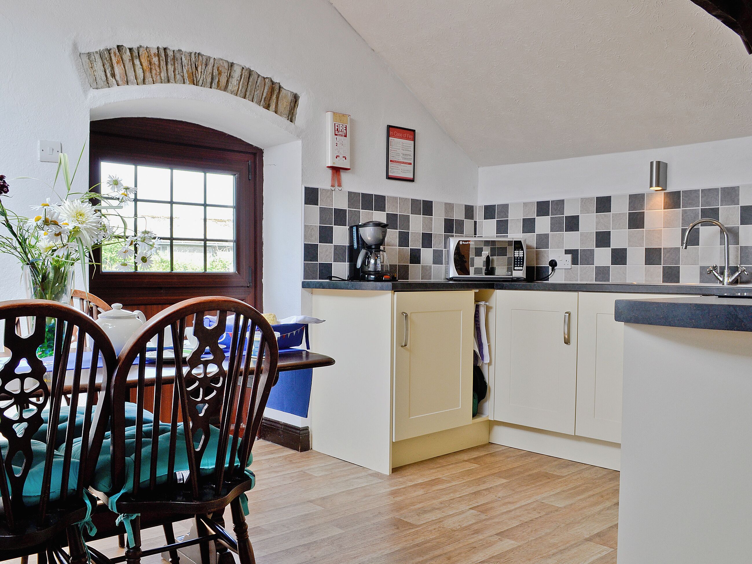 A kitchen with a microwave, coffee maker, and a sink. There is a window with a view outside, and a door leading to another room.