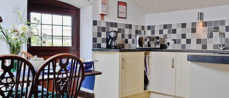A kitchen with a microwave, coffee maker, and a sink. There is a window with a view outside, and a door leading to another room.
