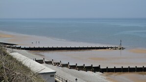 A coastal view with a concrete walkway leading to a sandy beach, a wooden breakwater, and a rocky shoreline. - 1 bedroom accommodation in Aylsham (Aylsham)