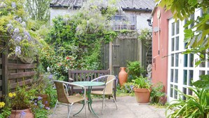 A patio with a table and chairs, surrounded by potted plants and a wooden fence. - 1 bedroom accommodation in Aylsham (Aylsham)