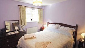 A bedroom with a bed, a dresser, a mirror, a window with curtains, and a bedside lamp. - 1 bedroom accommodation in Aylsham (Aylsham)
