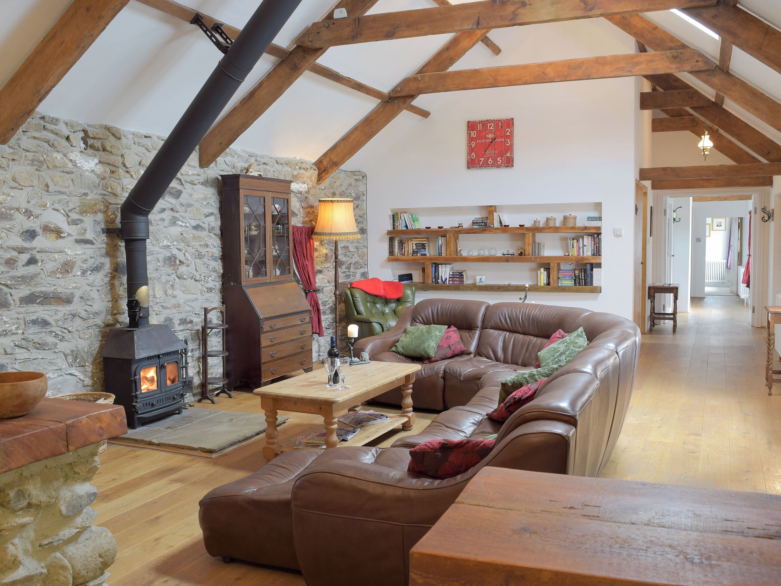 A cozy living room with a stone wall, wooden beams, a leather sofa, a wooden table, and a fireplace.