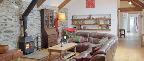 Un salón acogedor con pared de piedra, vigas de madera, un sofá de cuero, una mesa de madera y una chimenea.