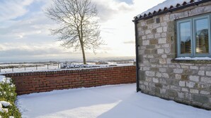 Schneebedeckte Landschaft mit einer Ziegelmauer und einem Steinhaus mit einem Fenster.
