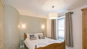 A bedroom with a wooden bed, two wall-mounted lights, a window with curtains, and a wardrobe. - Jorvik- Woodsmill Quay (Skeldergate, York)
