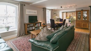 A living room with a green leather sofa, a wooden coffee table, and a bookshelf. There is a dining area with a table and chairs. - Jorvik- Woodsmill Quay (Skeldergate, York)