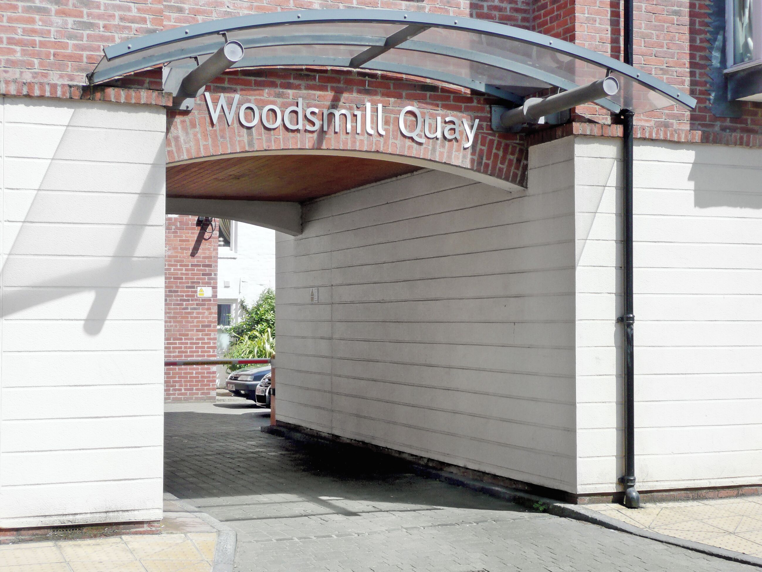 A building entrance with a sign reading "Woodsmill Quay" and a covered driveway.